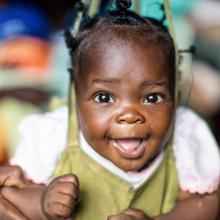 A baby smiles as she gets weighed